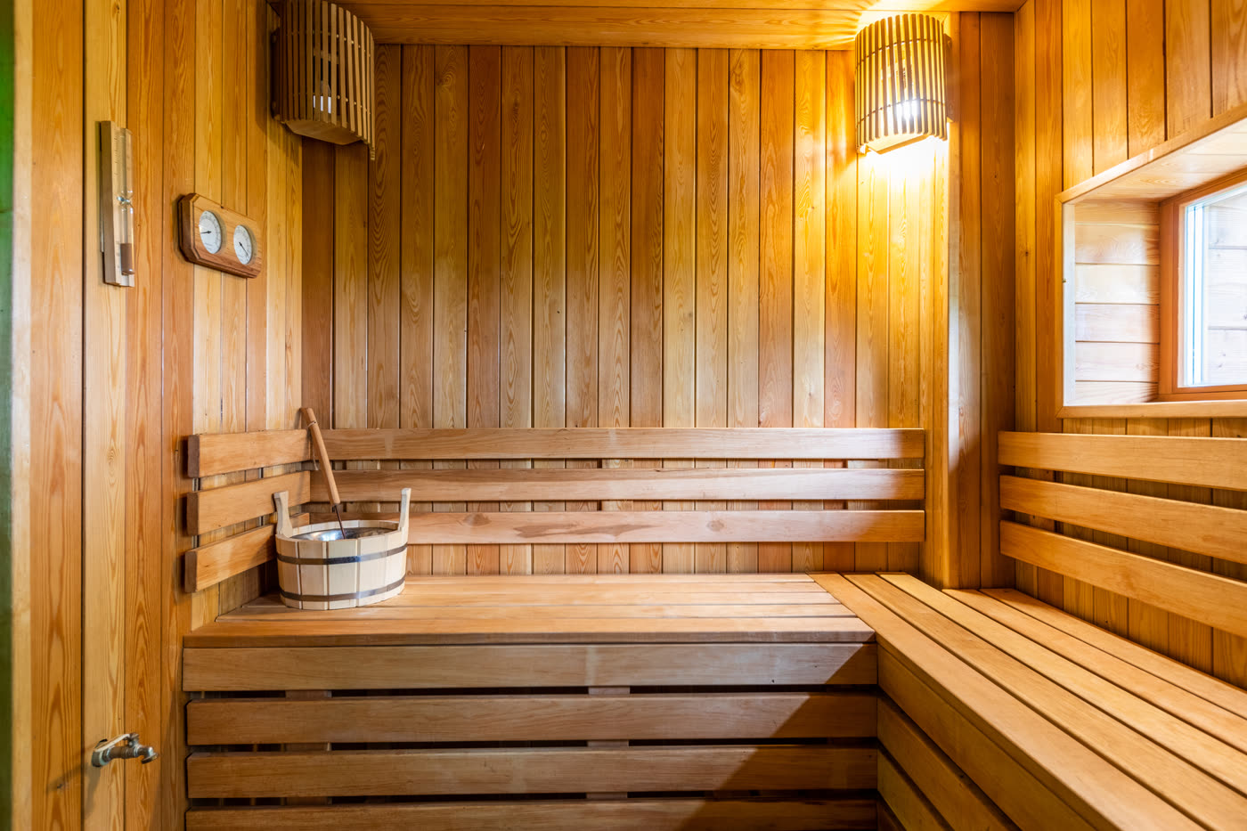 Wood sauna interior with benches and bucket.